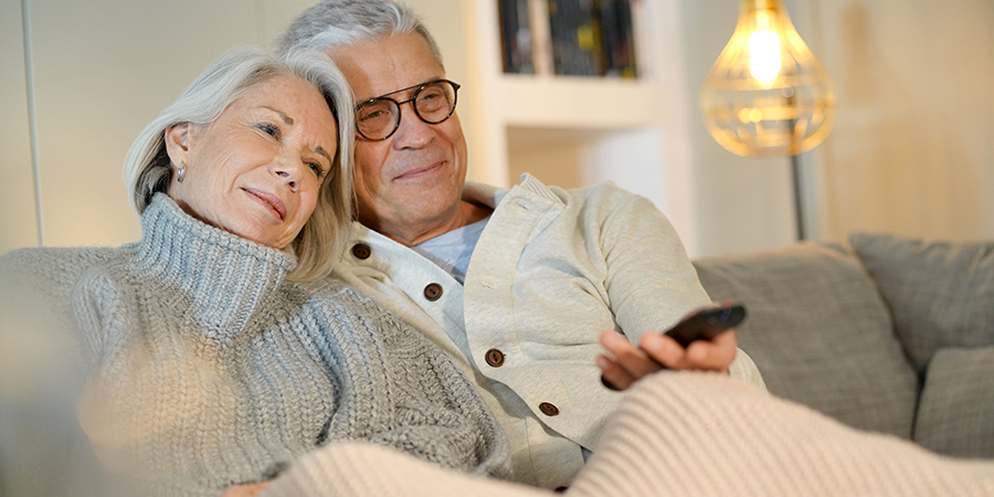 Senior couple at home relaxing on couch watching TV