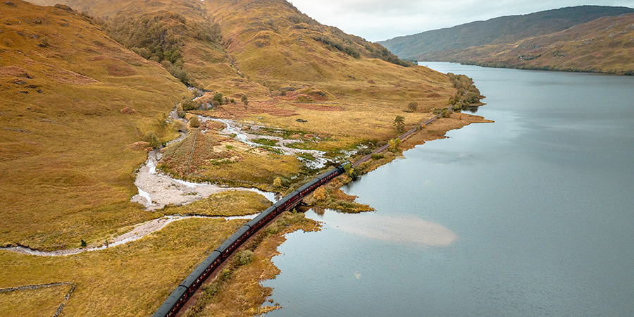 Steam Train Passing By A Loch And Mountains