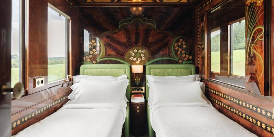 A beautifully decorated cabin on the Venice Simplon-Orient-Express: the room contains Art Deco details such as wood paneled walls with decorative flowers designs, patterned green furniture and golden details. 