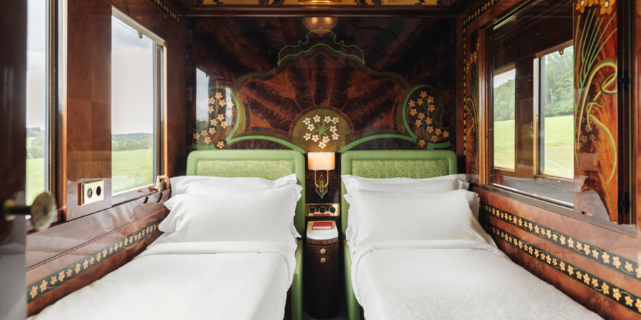 A beautifully decorated cabin on the Venice Simplon-Orient-Express: the room contains Art Deco details such as wood paneled walls with decorative flowers designs, patterned green furniture and golden details.